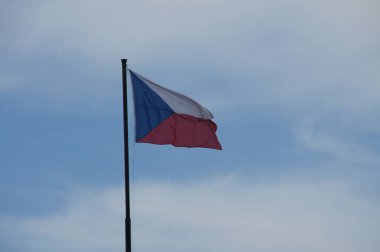 Çek Cumhuriyeti bayrağı, açık mavi gökyüzüne karşı rüzgarda gururla dalgalanıyor. Beyaz, mavi ve kırmızı çizgiler ülkenin zengin tarihini ve egemenliğini simgeliyor. Bu sembolik bayrak