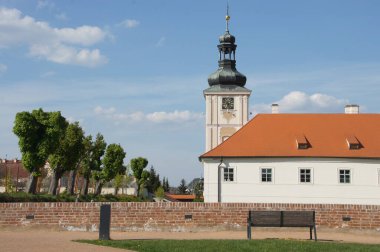 Cizvit Üniversitesi, Çek Cumhuriyeti. Kırmızı çatılı ve saat kulesi olan beyaz bina. Mavi gökyüzü ve bulutlarla güneşli bir gün. Tarihi dönüm noktası. Eğitim ve inancın sembolü. Cizvit Koleji, Çek Cumhuriyeti.