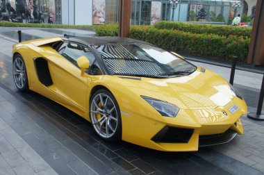 Dubai 'de, parlak sarı bir Lamborghini Aventador gökdelenin önünde görkemli bir şekilde dinlenir. Gösterişli İtalyan spor arabası şehrin lüks ve yüksek performanslı ruhunu temsil ediyor..