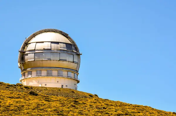 一架大望远镜在一座蓝天分明的山上 望远镜四周是长满青草的山坡 免版税图库图片