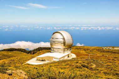 A large telescope is on a hill overlooking the ocean. The sky is clear and the sun is shining brightly clipart