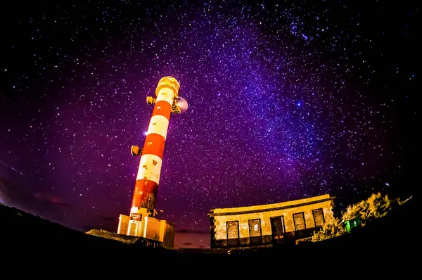 Stock image A lighthouse is lit up against a dark sky. The stars are shining brightly, creating a peaceful and serene atmosphere