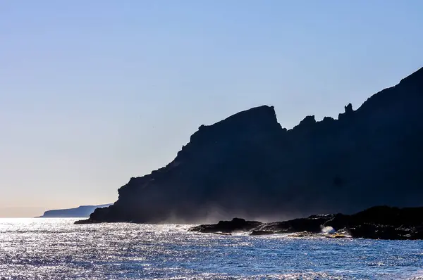 后背有悬崖的岩石海岸 天空是蓝色的 水是平静的 图库照片