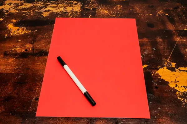 A red piece of paper with a black marker on it. The paper is on a wooden table