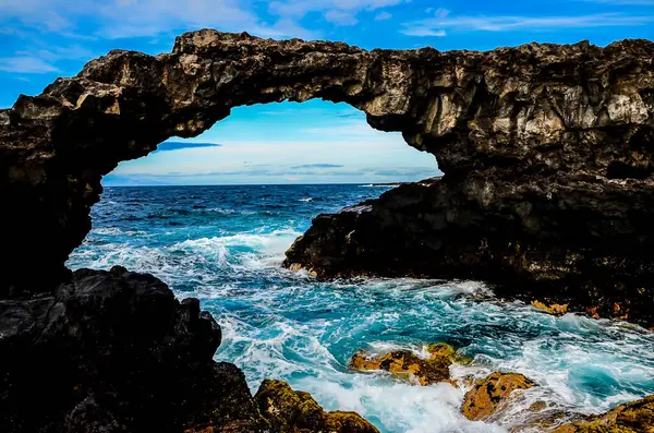 stock image A large archway is visible above the ocean, with the water crashing below. The archway is surrounded by rocks, and the ocean is a deep blue color. The scene is serene and peaceful, with the archway