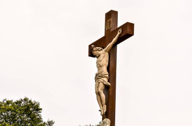 A cross with a statue of Jesus Christ on it. The statue is in a position that it is praying clipart