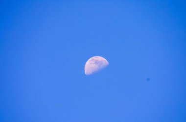 A large moon is in the sky above a blue sky. The moon is in the middle of the sky and is the only object visible clipart