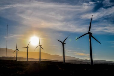 A group of wind turbines are silhouetted against a beautiful sunset. Scene is serene and peaceful, as the turbines stand tall and proud in the midst of a picturesque landscape clipart