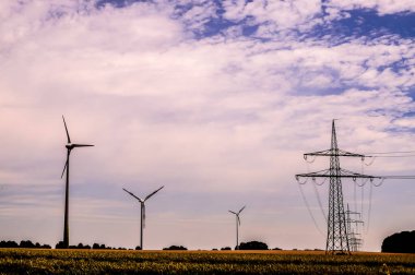 A field with a few wind turbines and a power line. The sky is cloudy and the mood is somewhat somber clipart