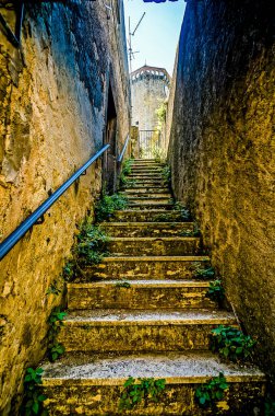 A narrow, steeply-rung staircase is shown in a narrow alleyway. The steps are made of stone and are covered in moss. Concept of mystery and intrigue clipart