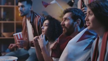 Karışık yarış hayranları oturma odasında kanepede oturup TV programı yarışma sporları şampiyonasını izliyorlar. Gergin insanlar favori takımı destekliyor ve gol bekliyorlar.