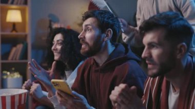 Heyecanlı futbol hayranları evde oturup TV 'de maç izliyor, online bahis için akıllı telefon uygulamasını kullanıyorlar. Futbol maçında zaferi kutlayan arkadaşlar