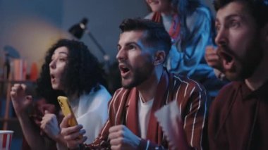 Heyecan verici bir an. Gençler TV ekranına bakıp yakınlarda çığlık atarken favori futbol takımı kazanıyor. Çok ırklı arkadaşlar kanepede oturup destek oluyorlar. Gerçek insan duyguları.