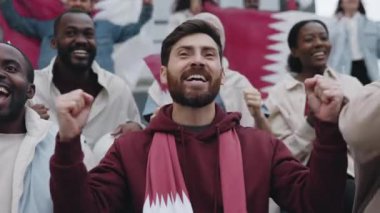 Yakışıklı sakallı adam tribünde çok ırklı kalabalığın arasında oturuyor ve futbol maçında duygusal olarak tezahürat yapıyor. Favori hobi, rekabet ve destek kavramı.