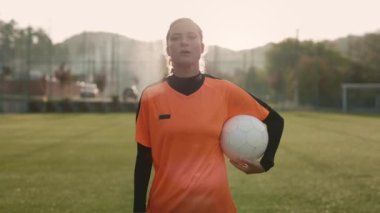 Dişi futbolcular. Spor Üniformalı Beyaz Kadın 'ın Stadyum' da dururken Beyaz Futbol Topu Tutarken Portresi. Kadın Futbolcu Sakin Yüzlü Kameraya Bakıyor
