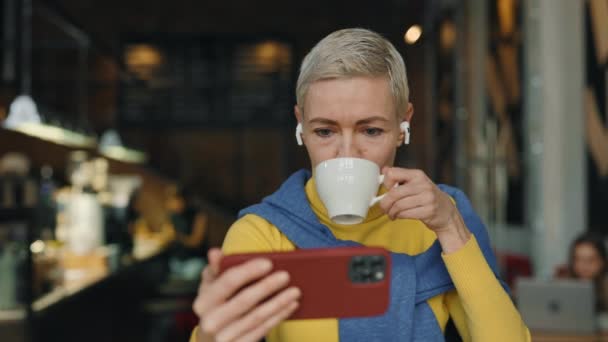 Biała Dojrzała Kobieta Siedząca Nowoczesnej Kawiarni Pijąca Kawę Oglądająca Filmy — Wideo stockowe