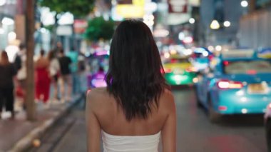 Gece Şehri 'ni Keşfeden Genç, Güzel Turist Kadın' ın Dönüşü. Cazibeli Kız Bustling Sokağı 'nın ortasında yürüyor, etrafa bakıyor. İnsanlar ve Seyahat Konsepti