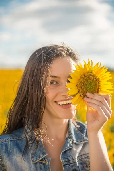 A young woman with a sunflower in front of her eyes in a field of sunflowers