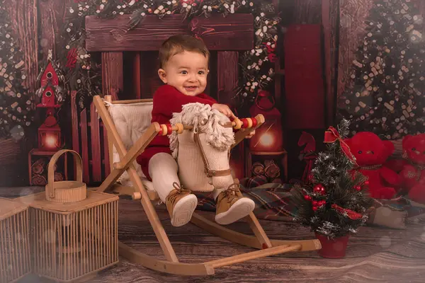 Küçük bir çocuk Noel sahnesinde oyuncak bir atın üzerinde oturuyor.