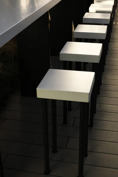 White modern counter stools lined up on the wooden deck
