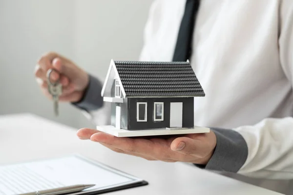 stock image Home insurance agent holding a house model and a key in the office. home loan insurance concept.