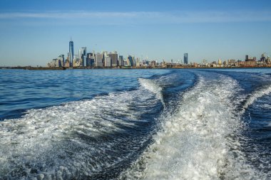 Hudson körfezinde dalgalar yaratan bir tekneden New York şehri panoraması.