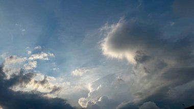 Gün batımındaki dramatik bir gökyüzünün nefes kesici görüntüsü, güneş ışınlarının karanlık bulutları delip geçmesi, ışık ve gölgenin çarpıcı bir kontrastını yaratıyor. Sakin atmosfer bir sükunet hissi uyandırıyor..