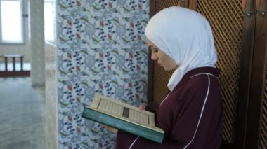 Musevi kız, elinde kutsal kitapla, camide Kur 'an okuyarak, Arap alfabesindeki kutsal dini kitabı okuyarak, Cami' ye dua ediyor.
