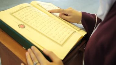 Arap alfabesi okuyor, İslam kitabından dualar okuyor, Arapça Kur 'an okuyor, Müslüman kız ahşap kürsüde sayfa çeviriyor.