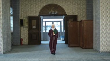 Camideki Müslüman kadın, gülümseyen ve tesettürlü mutlu Asyalı kadın, İslam kalplerini mutlu ediyor, güzel Müslüman kız camiye giriyor.