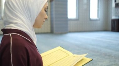 Arapça Alfabe okuyan, sayfaları çevirerek Kuran okuyan genç bir kız, Kuran okuyan tesettürlü Müslüman.