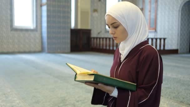 在清真寺祈祷的穆斯林女孩 手里拿着 古兰经 在清真寺里拜倒在伊斯兰头巾上的女孩 在清真寺里诵经 — 图库视频影像