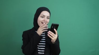 Müslüman kadın telefon şokuna bakıyor, yeşil ekranın önünde gülen siyah tesettürlü kız, genç insan telefon ekranını gördü çok mutlu.