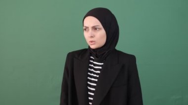 İzole edilmiş yeşil arka planda soğuk bir Müslüman kadın, kolunda ısınan bir kız, krom anahtar izole bir arka plan.