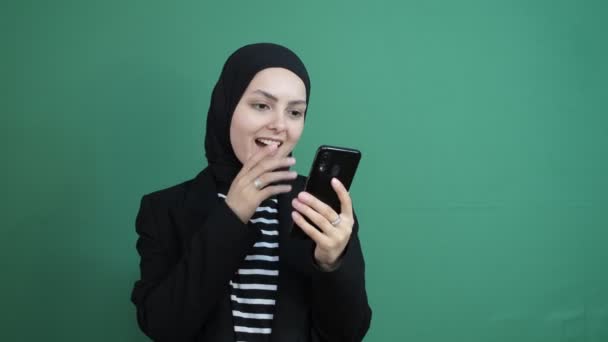穆斯林女人看着手机震惊了 笑着在绿色屏幕前的黑头巾女孩 年轻人看到手机屏幕是很开心的 — 图库视频影像