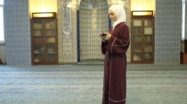 İslam İlmihal Uygulaması, camideki tesettürlü kızın elinde yeşil ekranı gösterme, telefonda İslam uygulamalarının tanıtımı 
