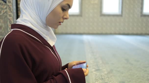 数字古兰经 中的女性祷告 穆斯林头巾女孩跟随手机屏幕上的Quran 在清真寺里礼拜 在清真寺里做穆斯林祷告 — 图库视频影像