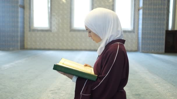 女孩朗诵 古兰经 年轻女孩坐在地板上朗诵昆兰文 穆斯林头巾女人从手中的昆兰书里祈祷 — 图库视频影像