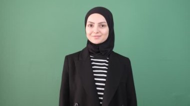 Müslüman bir kadın, yeşil ekranın önünde yatıyor, mutlu hissediyor, dişlerini göster.