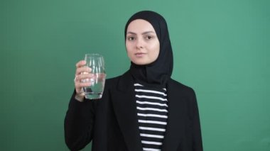 Müslüman kadın su içiyor, kız yeşil ekranın önünde su imzalıyor, vücudundan mineral alıyor genç insan, içme suyu için sağlıklı yaşam, izole edilmiş yeşil arka plan