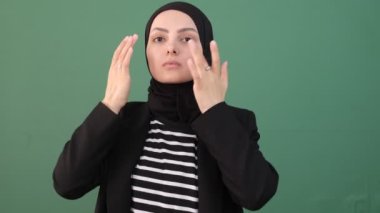 Kadın kendine çeki düzen verir, kız yeşil arka planı temizler, kendine çeki düzen verir, eşarbını ve yüzünü gösterir. 