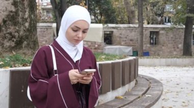 Beyaz kız dışarıda mesajlaşıyor, tesettürlü kız caminin avlusunda telefonuna bakıyor sosyal medyayı kullanan Müslüman, dünyayla bağlantı kuruyor.