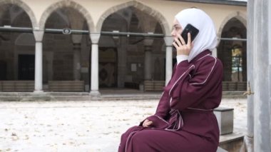 Kafkas Kız Konuşan Telefonu, tesettürlü kız telefon ekranı gösteriyor, cami avlusunda zaman geçiriyor, çevrimiçi teknoloji İslam uygulamasında.