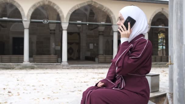 白人の女の子の話電話 携帯電話の画面を示すヒジャーブの女の子 モスクの中庭で時間を過ごす イスラム教のアプリケーションでオンライン技術 — ストック動画