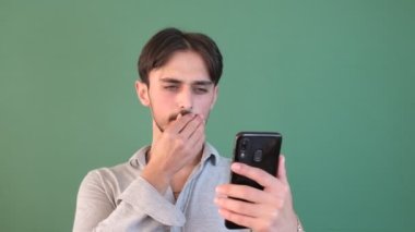 Gülümseyen adam yeşil ekranı işaret ediyor, genç, sıradan görünümlü, izole edilmiş yeşil arka planın önündeki telefon ekranını işaret ediyor. 