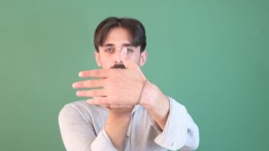 Sakallı genç adam elinin arkasını işaret ederek kroma anahtarının önünde, gülümseyerek parmağını hediye gibi gösteriyor.