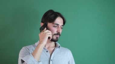 Konuşan genç beyaz adam gülümsüyor yeşil ekranın önünde akıllı telefondan konuşuyor, insanlar konuşmak için telefon kullanıyor.