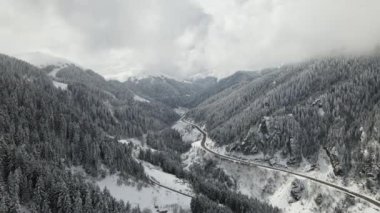 Karlı kış gününde karlı ormanın içinden geçen otoyolun hava manzarası, karlı dağların arasından geçen gökyüzü manzarası, kış soğuk.