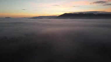 Ufuktaki uzak dağlarla beyaz kabarık bulutların üzerinde sarı günbatımının hava manzarası, güzel bir gün doğumu.