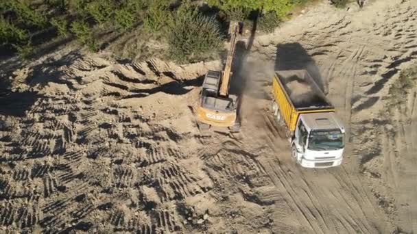 庭園近くの砂田の容器に砂をロードするバックホウトラックの空中ビュー 建設機械は土を掘ることによって動作します — ストック動画